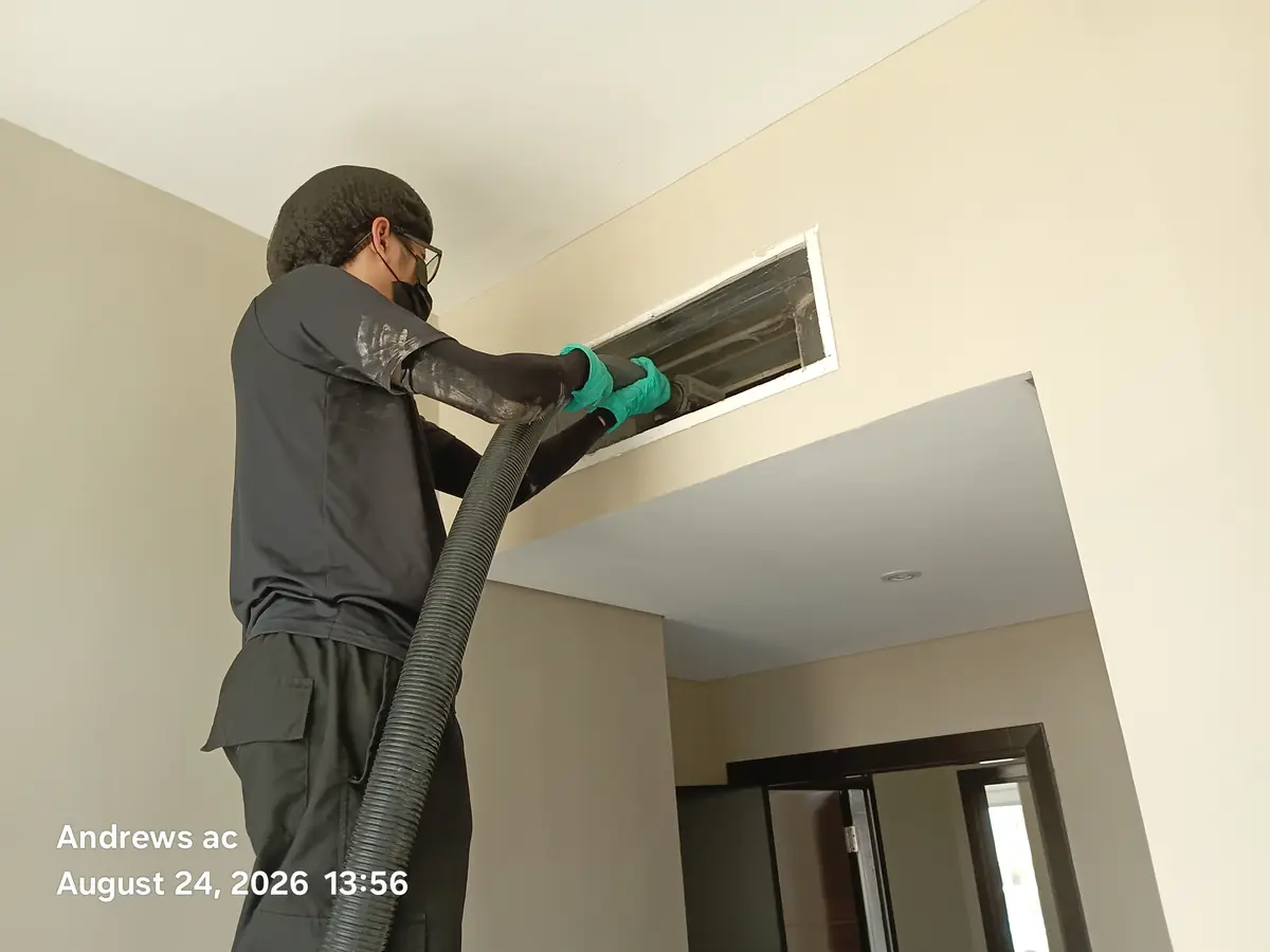 Andrews AC technician vacuuming dust out of an open ceiling air conditioning vent