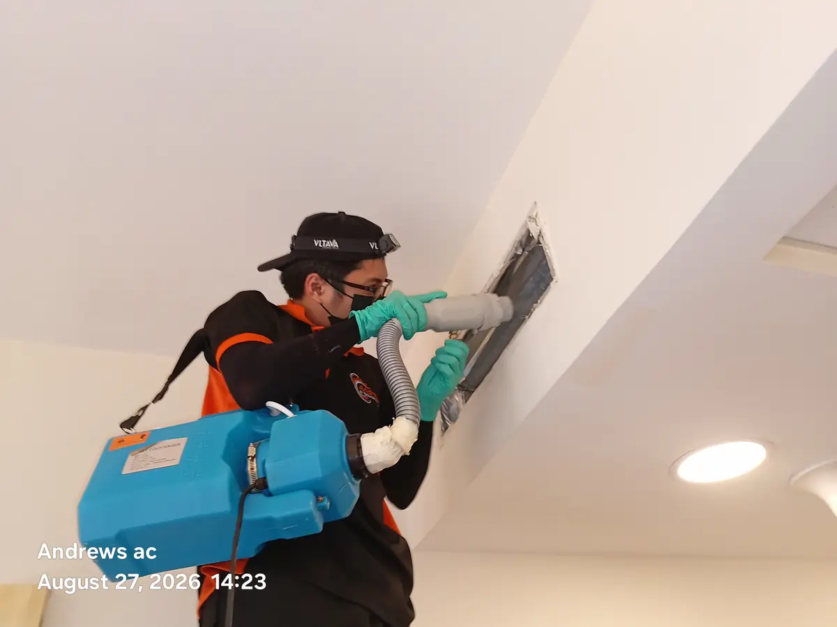 Andrews AC technician in gloves and mask directing a cold fogger into an open ceiling duct to disinfect it